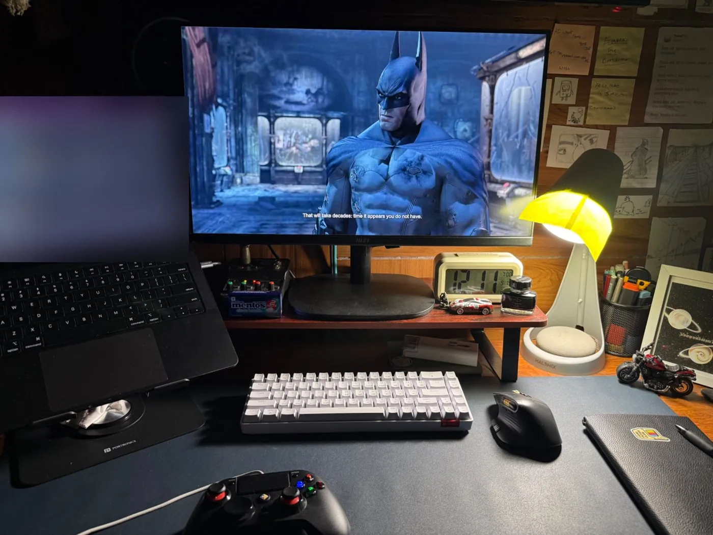 my desk at night: MSI monitor, Halonix lamp, clock, Hydra 10 keyboard, Amkette mouse, Cosmic Byte controller. the laptop screen is blurred.